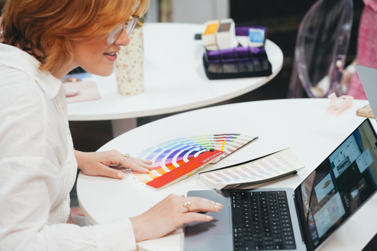 Graphic designer sitting at a desk working on her computer and looking through samples of pantone colors.