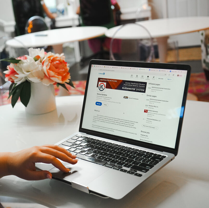 A laptop sitting on a desk in agency office with the wastewater company's LinkedIn social media on the screen and a vase with flowers on the desk.